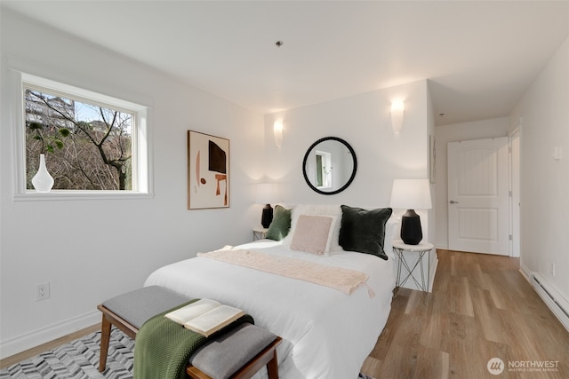 bedroom featuring a baseboard heating unit, baseboards, and light wood finished floors