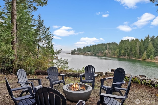 view of patio featuring a forest view, a water view, and a fire pit