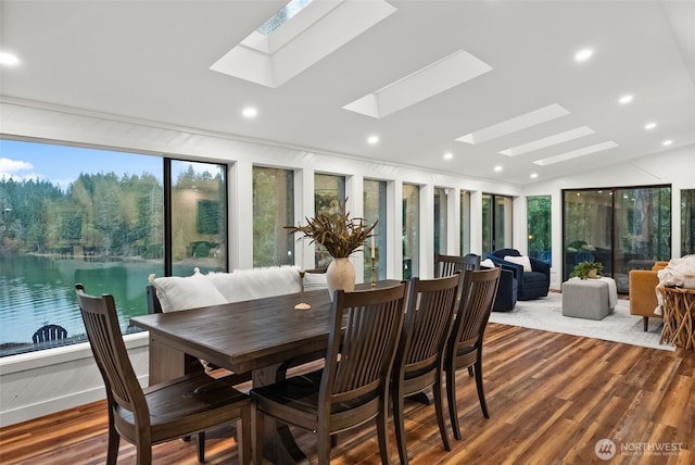 dining area with recessed lighting, vaulted ceiling with skylight, wood finished floors, and a water view