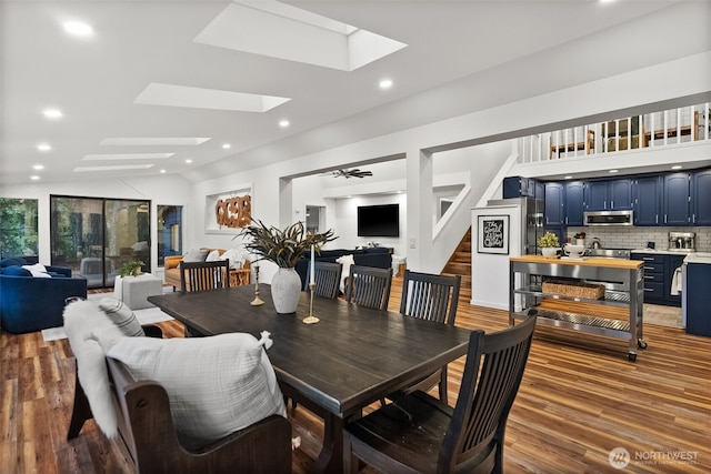 dining room with vaulted ceiling with skylight, stairway, recessed lighting, and wood finished floors