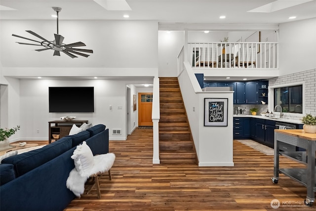 living room featuring stairway, dark wood-style floors, a skylight, a high ceiling, and recessed lighting