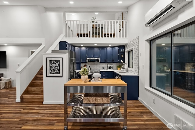 kitchen with blue cabinets, visible vents, a wall mounted AC, appliances with stainless steel finishes, and dark wood-style flooring