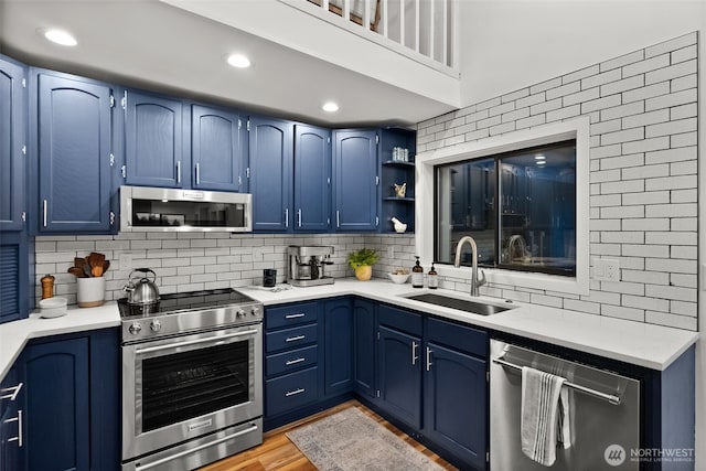 kitchen with blue cabinets, a sink, open shelves, appliances with stainless steel finishes, and light countertops