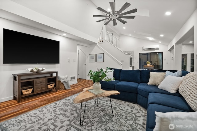 living room featuring stairway, wood finished floors, a ceiling fan, high vaulted ceiling, and a wall mounted AC