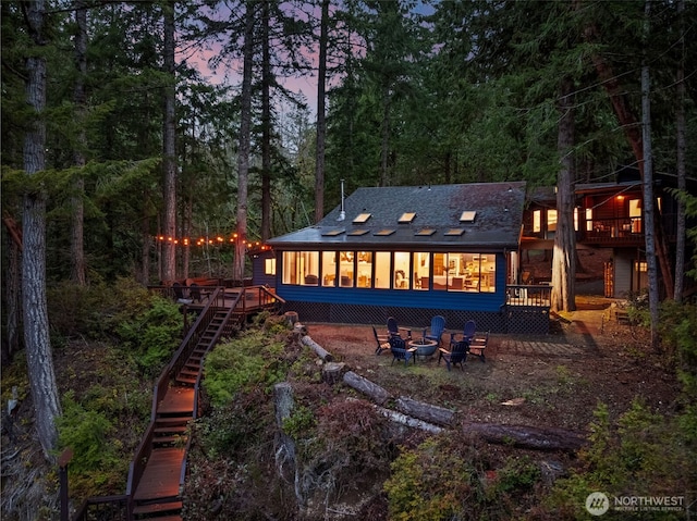 back of property at dusk with a wooden deck, stairway, a fire pit, and a sunroom