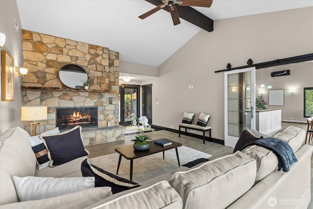 living area featuring beam ceiling, a stone fireplace, wood finished floors, and a ceiling fan