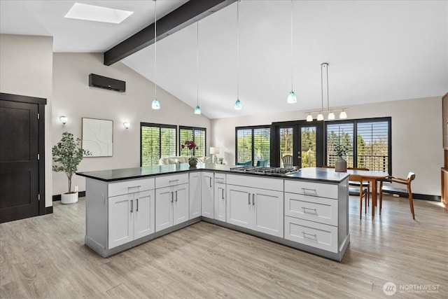 kitchen featuring beam ceiling, a skylight, light wood-style flooring, stainless steel gas stovetop, and dark countertops