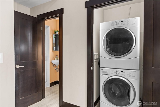 laundry area with laundry area, light wood-style floors, baseboards, and stacked washing maching and dryer