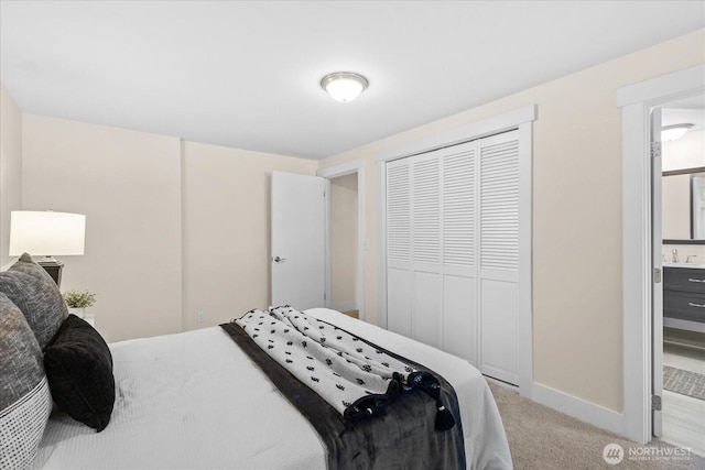 bedroom with baseboards, light carpet, a closet, ensuite bath, and a sink