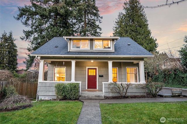 bungalow-style house with a porch, a shingled roof, a front lawn, and fence