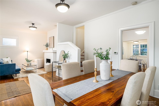 dining space featuring a fireplace, stairway, and wood finished floors