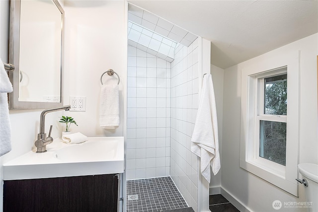 bathroom with vanity, toilet, baseboards, and a tile shower