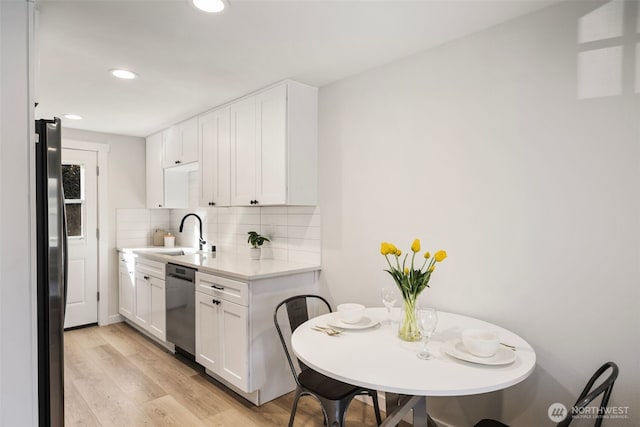 kitchen with tasteful backsplash, light countertops, light wood-style flooring, appliances with stainless steel finishes, and a sink