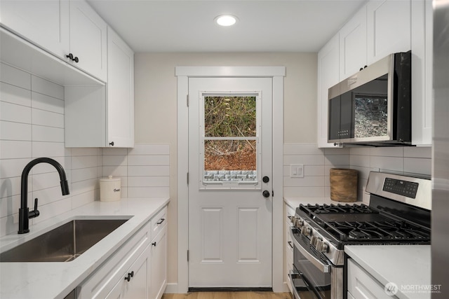 kitchen with tasteful backsplash, light stone countertops, white cabinets, stainless steel appliances, and a sink