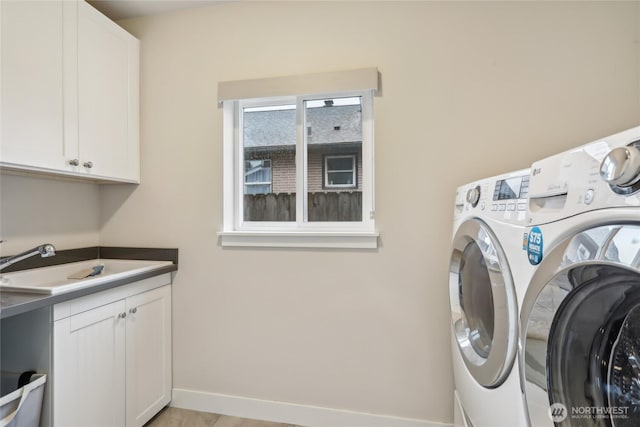 laundry room featuring a sink, baseboards, cabinet space, and separate washer and dryer