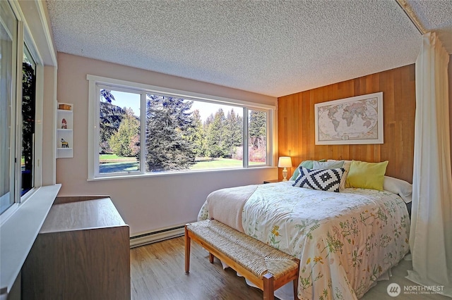 bedroom featuring a baseboard radiator, wooden walls, wood finished floors, and a textured ceiling