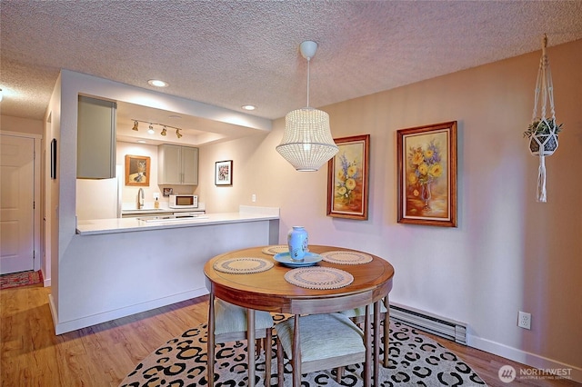 dining space featuring a baseboard heating unit, baseboards, a textured ceiling, and light wood finished floors