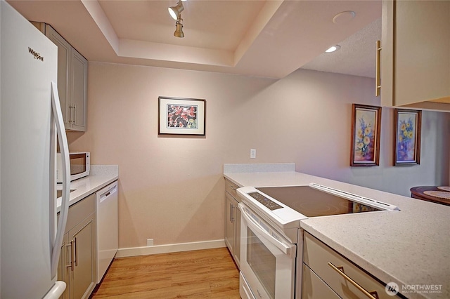 kitchen with white appliances, baseboards, a tray ceiling, light countertops, and light wood-type flooring