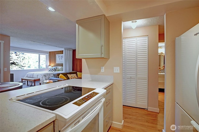 kitchen featuring white appliances, light wood-style flooring, light countertops, a textured ceiling, and open floor plan