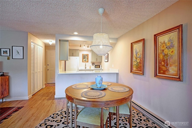 dining area with baseboards, a textured ceiling, and light wood finished floors