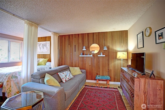 living room featuring baseboards, wooden walls, wood finished floors, and a textured ceiling