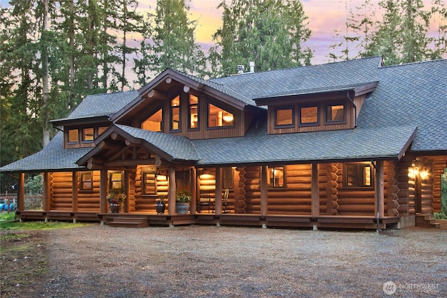 back of house at dusk with roof with shingles and log exterior