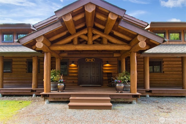 view of exterior entry featuring log siding, a porch, and roof with shingles