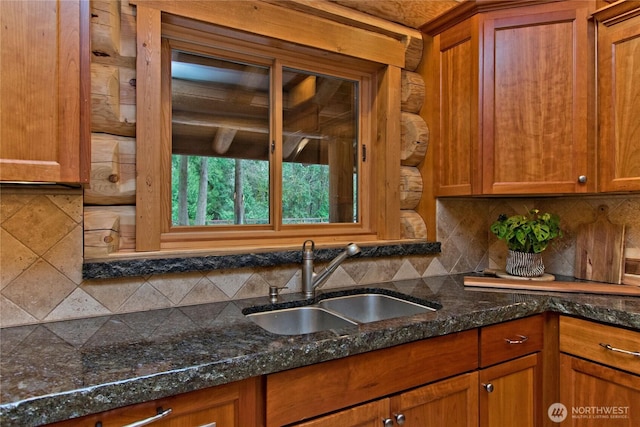 kitchen featuring brown cabinetry, backsplash, dark stone counters, and a sink