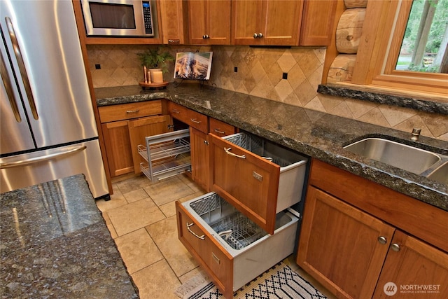 kitchen with decorative backsplash, dark stone counters, brown cabinetry, and stainless steel appliances