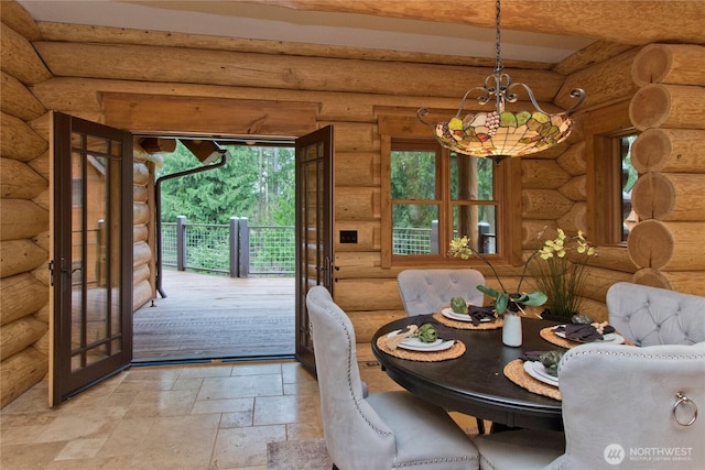 unfurnished dining area with an inviting chandelier, stone tile floors, french doors, and rustic walls