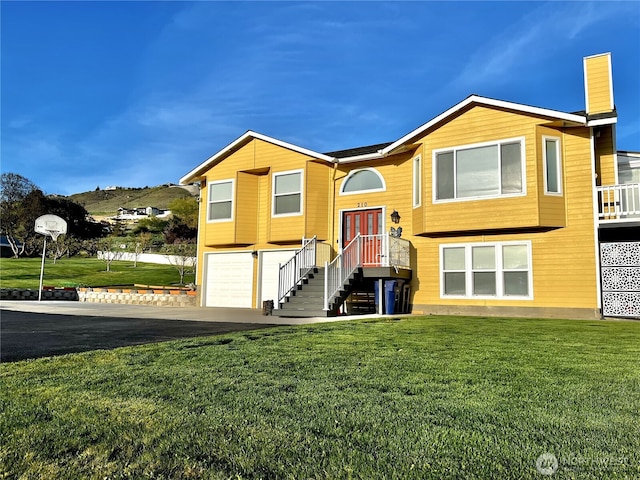 split foyer home featuring an attached garage, a chimney, driveway, and a front yard