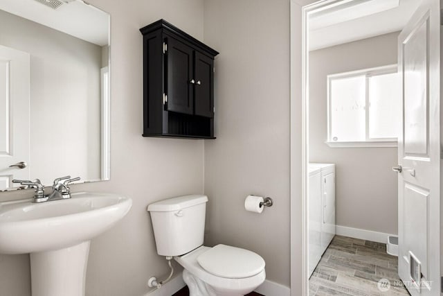 bathroom featuring washing machine and clothes dryer, toilet, baseboards, and wood finished floors