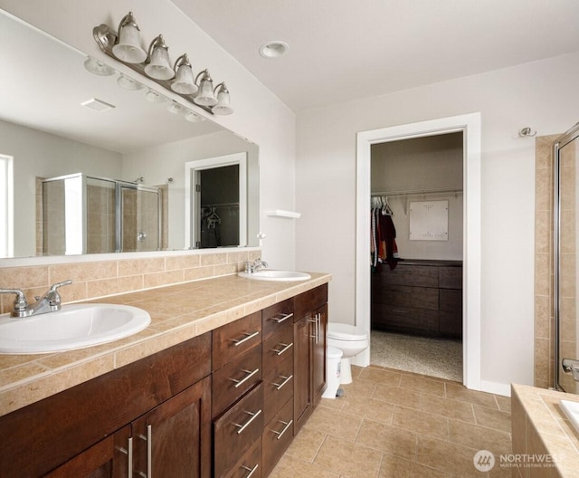 bathroom with a spacious closet, a shower stall, double vanity, and a sink