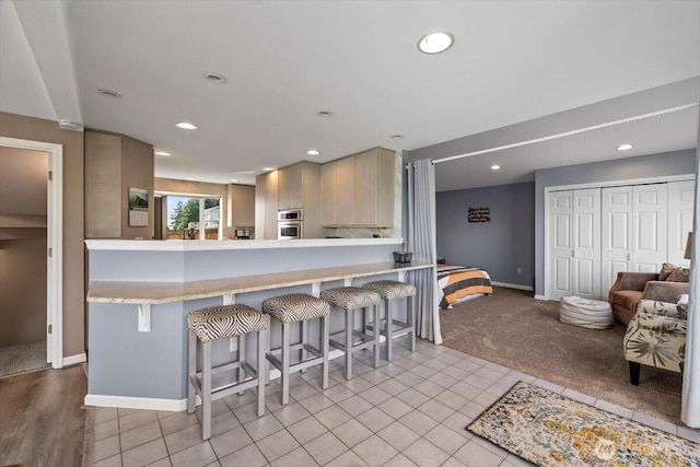 kitchen featuring stainless steel oven, a breakfast bar, recessed lighting, and light countertops