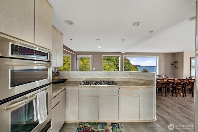 kitchen with light wood-type flooring, cream cabinetry, recessed lighting, appliances with stainless steel finishes, and a peninsula