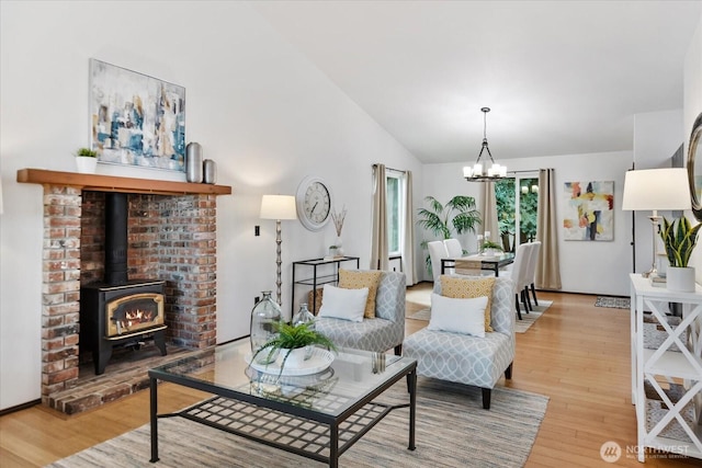 living area with a wood stove, light wood-type flooring, an inviting chandelier, and vaulted ceiling