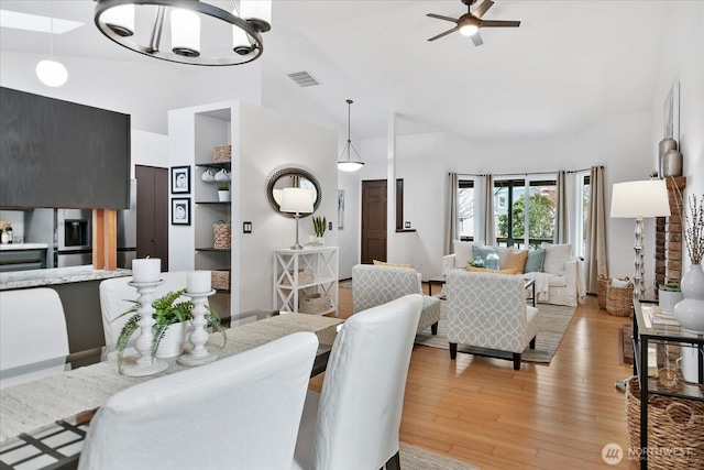 dining room featuring high vaulted ceiling, ceiling fan with notable chandelier, visible vents, and light wood-type flooring