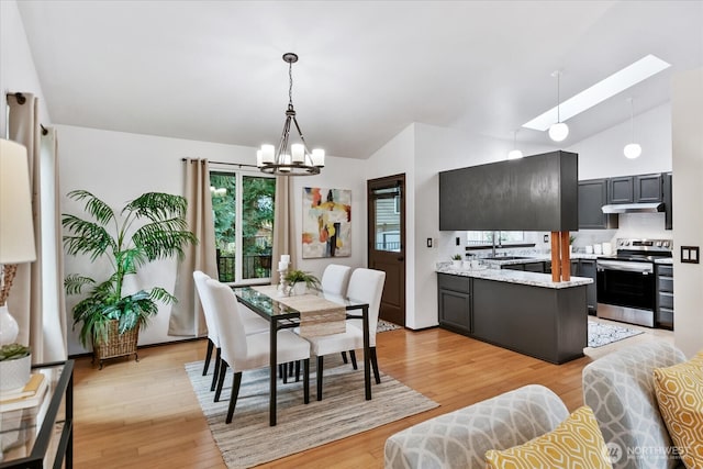 dining area with a notable chandelier, a skylight, light wood-style floors, and high vaulted ceiling