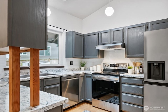 kitchen featuring light stone counters, hanging light fixtures, light wood-style floors, under cabinet range hood, and appliances with stainless steel finishes