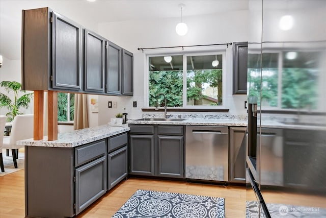 kitchen with a sink, plenty of natural light, a peninsula, light wood finished floors, and dishwasher