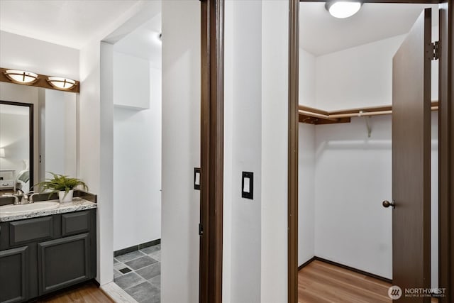 bathroom with vanity, a spacious closet, wood finished floors, and baseboards