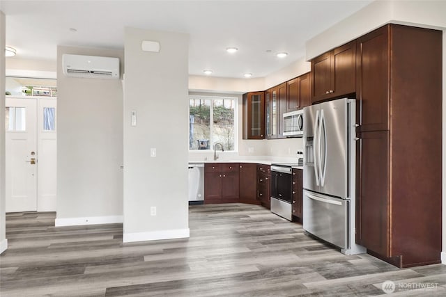 kitchen featuring a wall mounted AC, a sink, appliances with stainless steel finishes, light wood finished floors, and glass insert cabinets