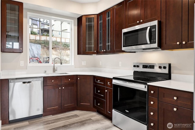 kitchen with light wood finished floors, a sink, light countertops, glass insert cabinets, and appliances with stainless steel finishes