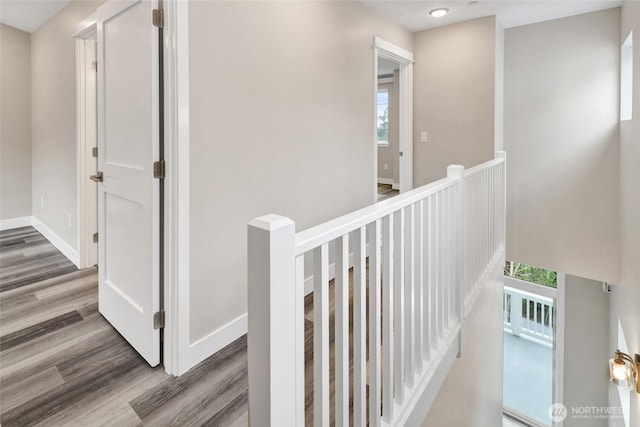 corridor featuring baseboards, an upstairs landing, and wood finished floors