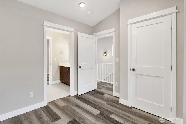 unfurnished bedroom with dark wood-style floors, baseboards, ensuite bath, and lofted ceiling