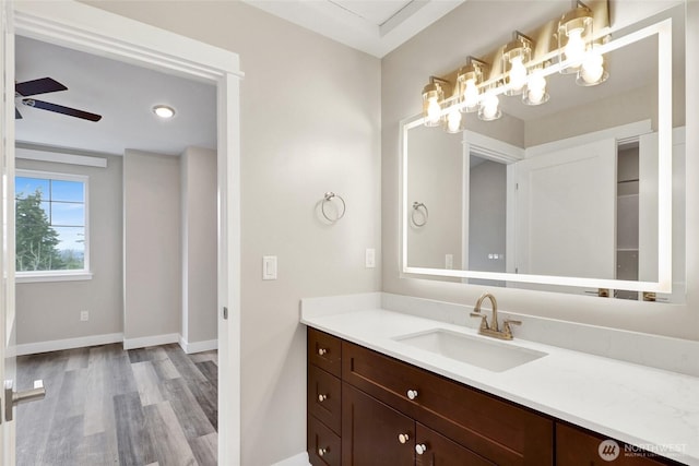 bathroom with ceiling fan with notable chandelier, vanity, baseboards, and wood finished floors