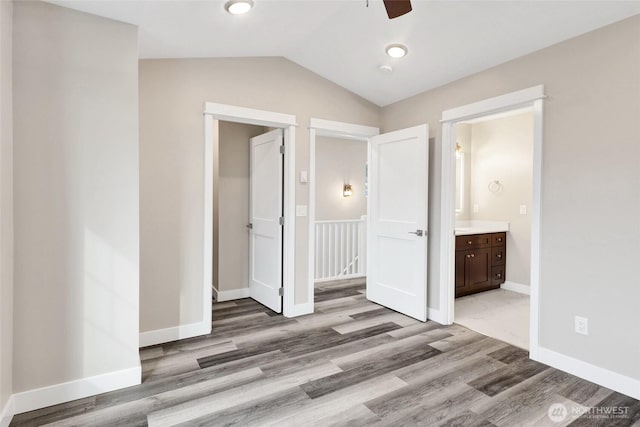 unfurnished bedroom featuring connected bathroom, wood finished floors, baseboards, and vaulted ceiling