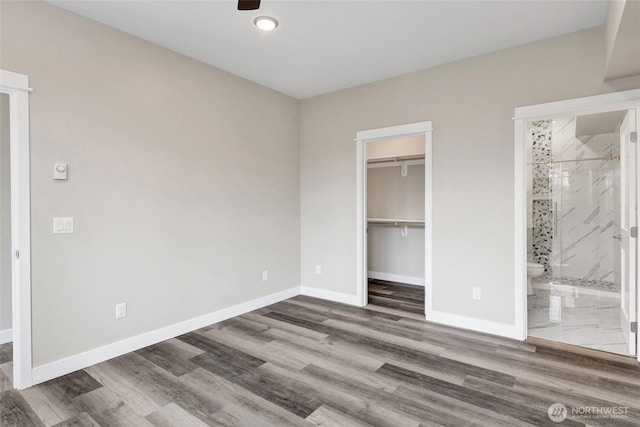 unfurnished bedroom with connected bathroom, a walk in closet, baseboards, wood finished floors, and a closet