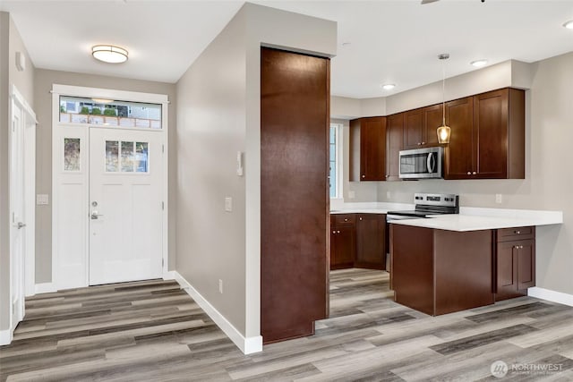 kitchen with stainless steel microwave, light countertops, light wood-type flooring, and a peninsula