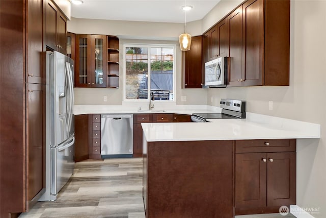 kitchen with glass insert cabinets, light wood-style flooring, a peninsula, stainless steel appliances, and a sink